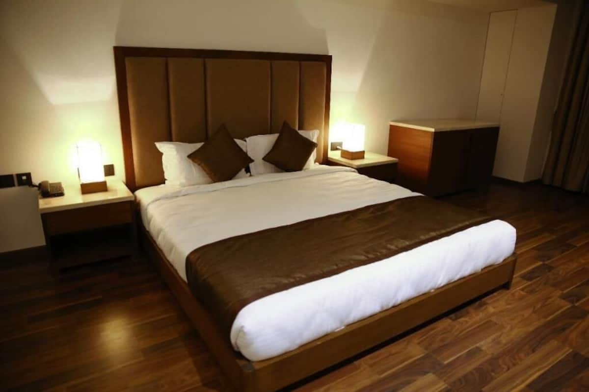A hotel room with a large bed, wooden headboard, two bedside tables with lamps, and a wooden floor.