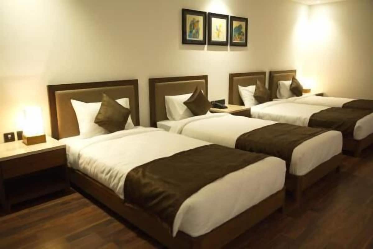 A hotel room with four single beds, wooden headboards, white bedding, and a nightstand with a lamp.