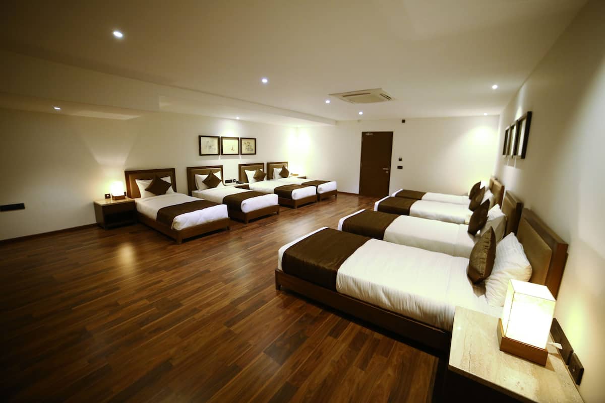 A hotel room with four beds arranged in a row, wooden flooring, and a door in the background.