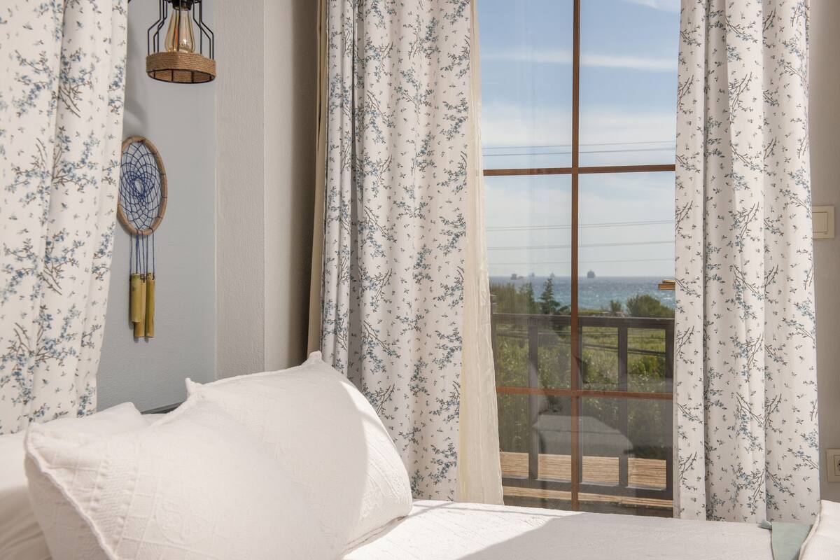 Une chambre avec une grande fenêtre, un lit recouvert de draps blancs et une décoration murale.