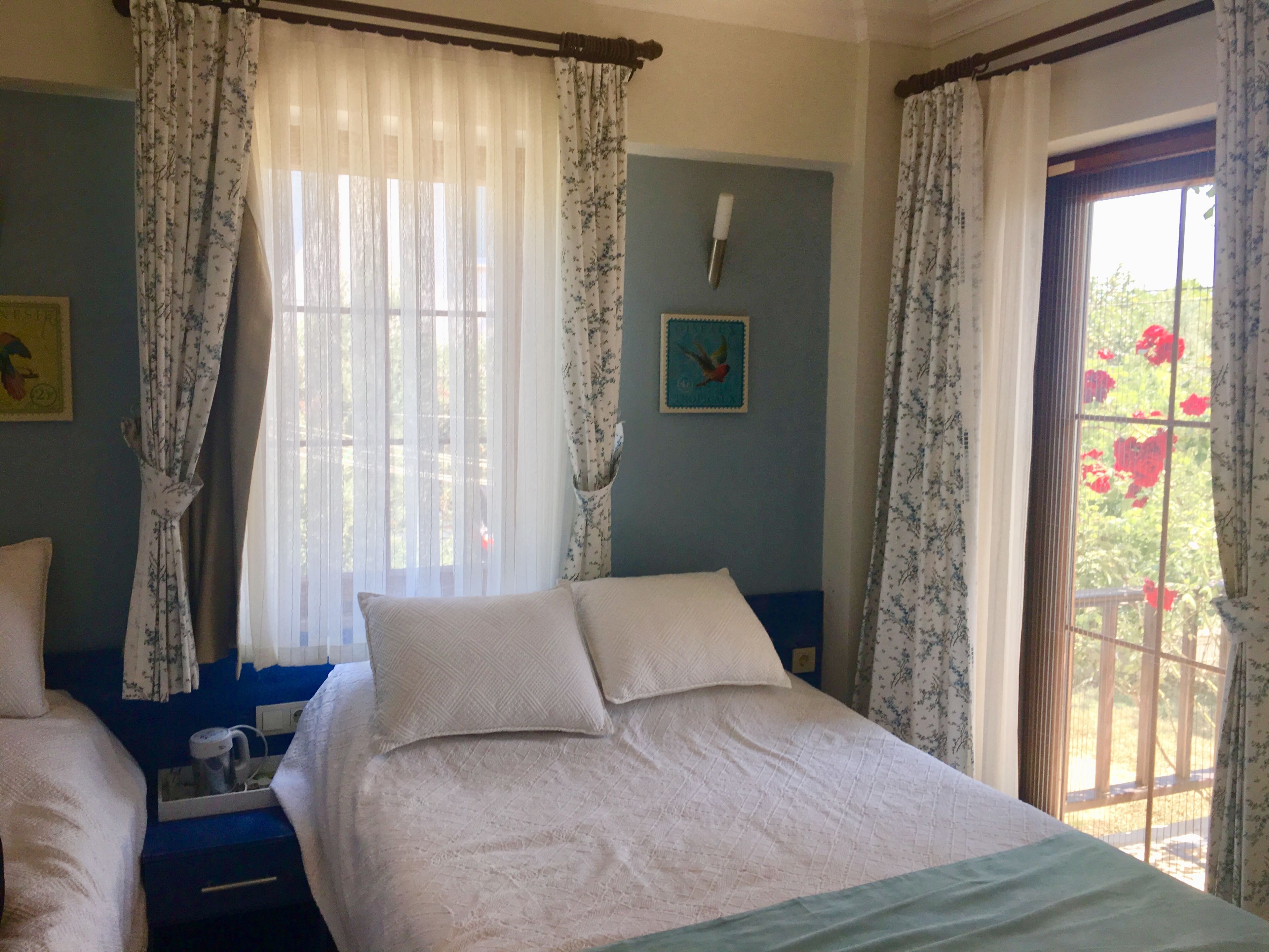 A bedroom with a bed, a bedside table, a window with curtains, and a wall clock.