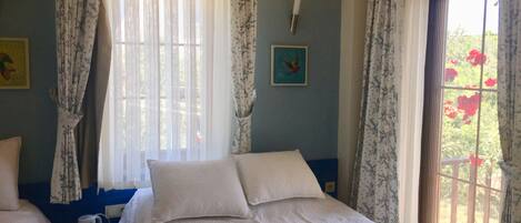 A bedroom with a bed, a bedside table, a window with curtains, and a wall clock.