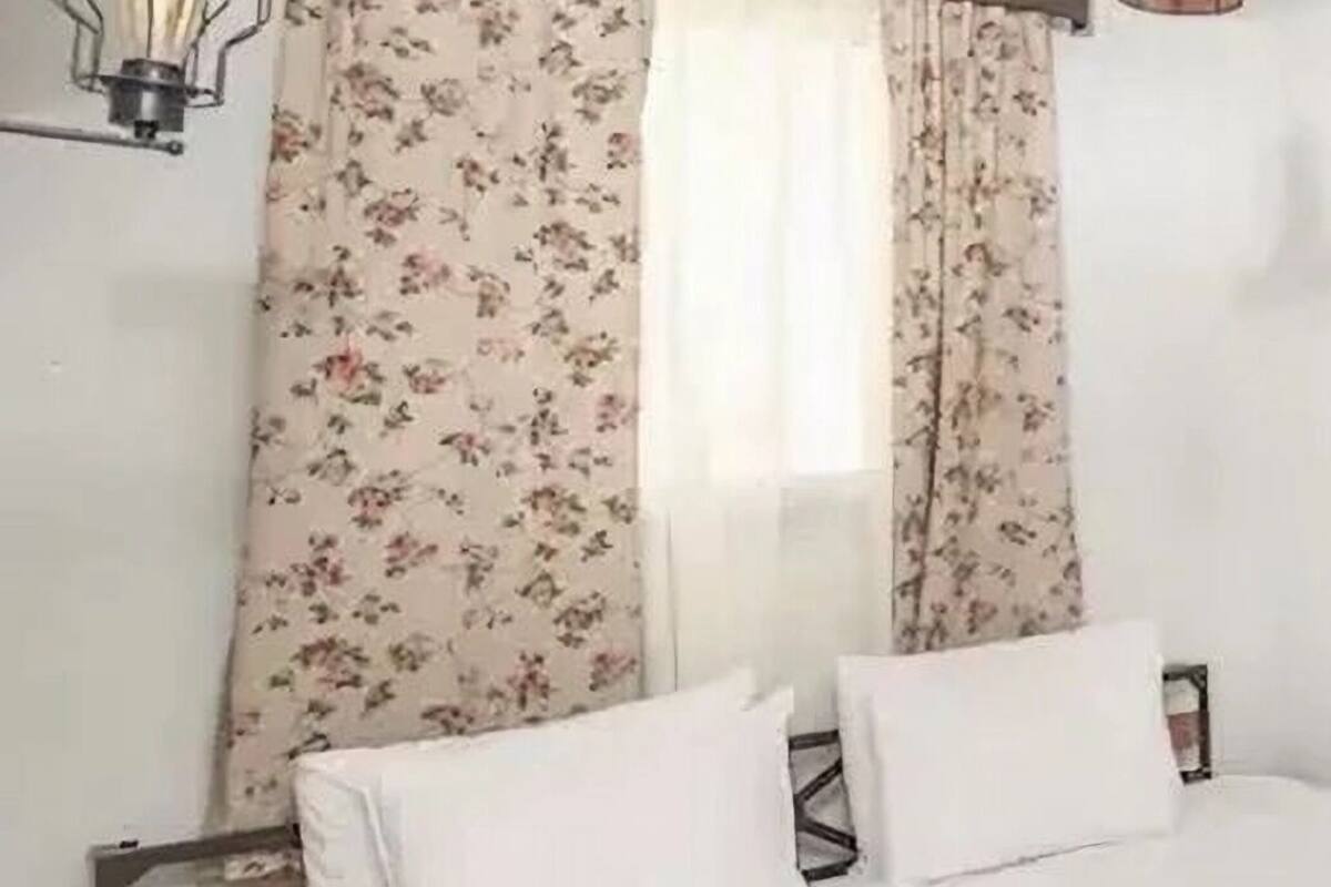 Une chambre à coucher avec un lit, des rideaux à motifs floraux, un luminaire suspendu et une table de chevet.