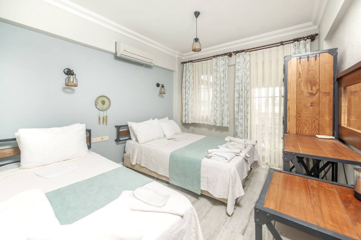 Une chambre d’hôtel avec deux lits, une table en bois et une fenêtre avec des rideaux.
