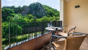 A balcony with wicker chairs, a small table, and a view of a forested mountain. - Hotel Ruland (Altenahr)