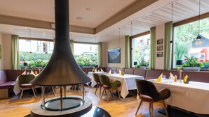 A restaurant with a central black conical structure, wooden flooring, and a view of greenery outside. - Hotel Ruland (Altenahr)