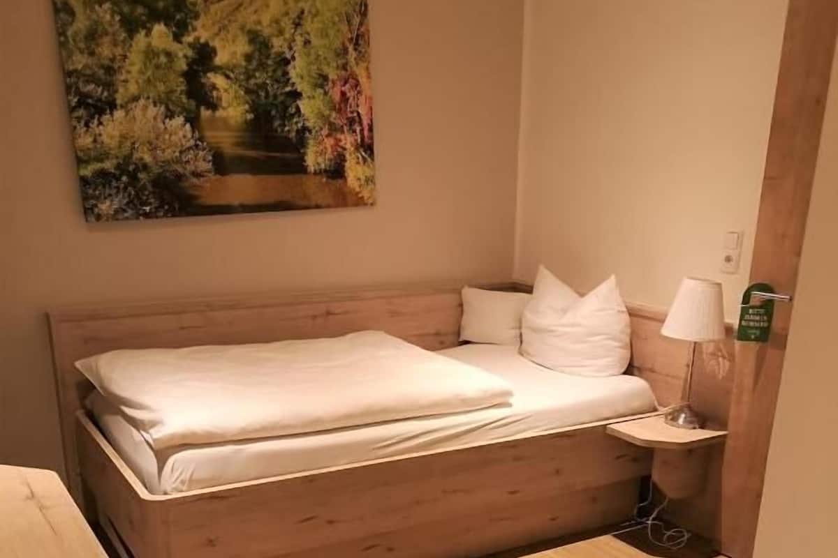 Ein Schlafzimmer mit einem hölzernen Bett, weißer Bettwäsche, einem Nachttisch mit Lampe und einem Gemälde an der Wand.