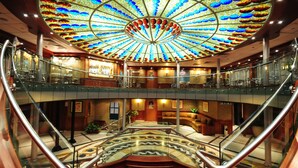Ein mehrgeschossiges Atrium mit Glastrennwand, einer zentralen Treppe und einem lebendigen Deckendesign.