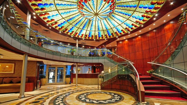 Eine beeindruckende Lobby mit kreisförmigem Boden, einer zentralen Treppe und einer farbenfrohen Glasdecke.