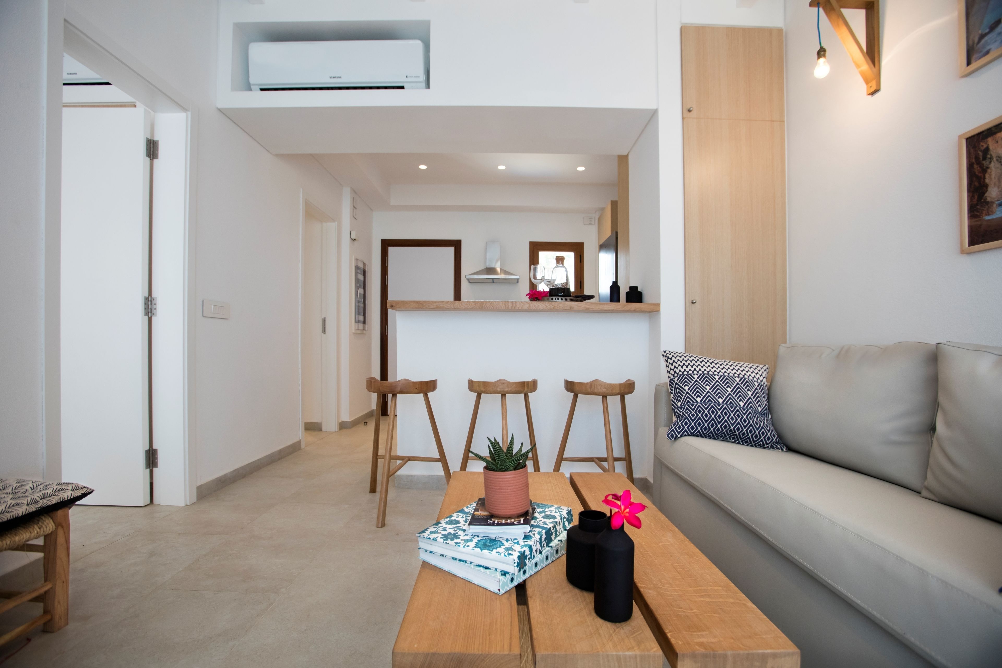 A modern living room with a wooden coffee table, a sofa, and a kitchen area in the background.