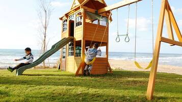 Children can play in the playhouse with a slide and swing set on the grassy area near the beach.