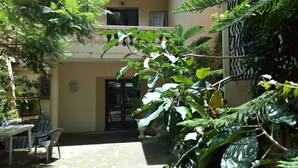 Un patio con una mesa y sillas, rodeado de abundante vegetación y un edificio con balcón.