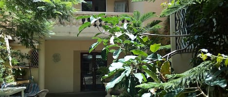 A courtyard with a table and chairs, surrounded by lush greenery and a building with a balcony.