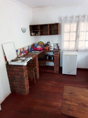 Eine kompakte Küche mit Gasherd, kleinem Kühlschrank und einer Ablage für Geschirr.