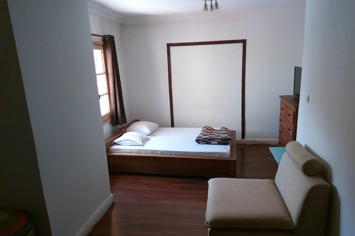 Ein kleines, ordentlich eingerichtetes Schlafzimmer mit einem Einzelbett, einem hölzernen Schminktisch und einer kleinen Couch.