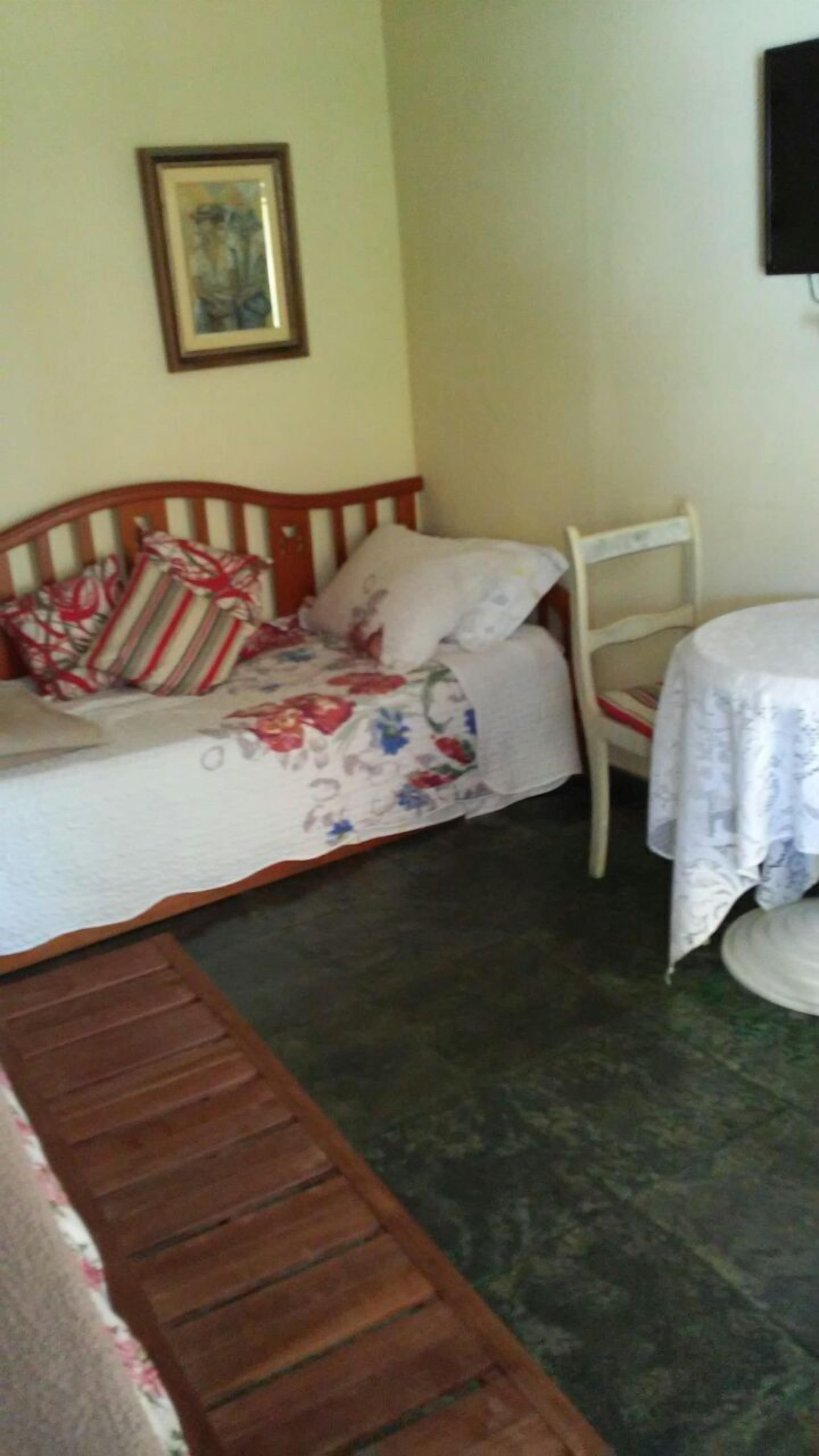 A bedroom with a bed, a chair, a table, and a wall-mounted TV.