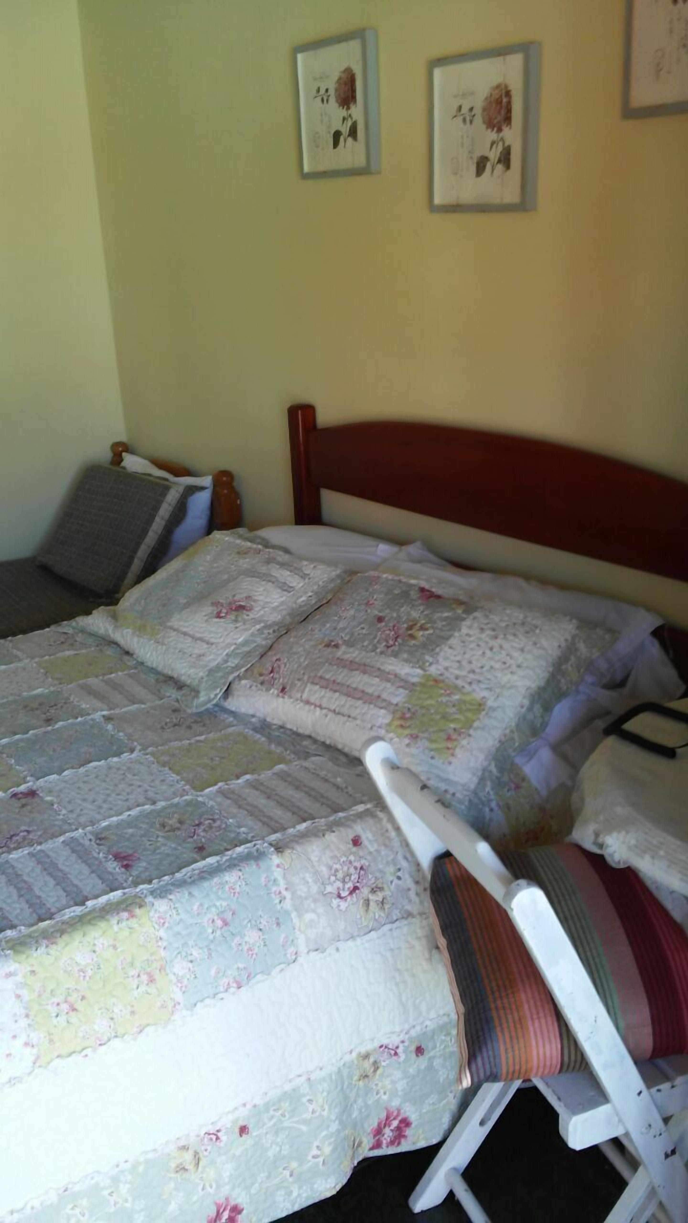Una cama con colcha estampada, cabecera de madera y mesita de noche con lámpara.