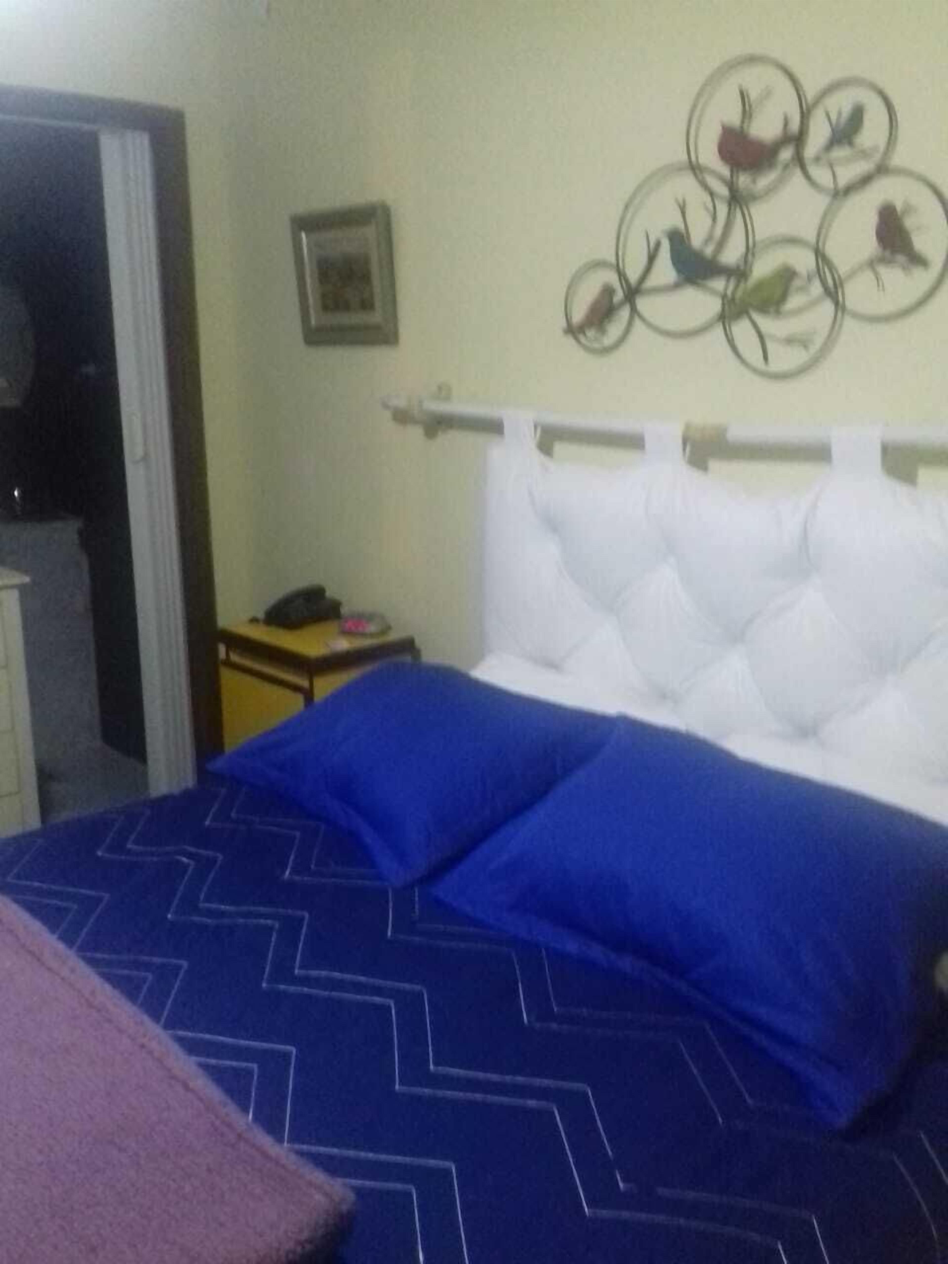 Un dormitorio con una cama que tiene una colcha azul estampada y un cabecero blanco con capitonado.