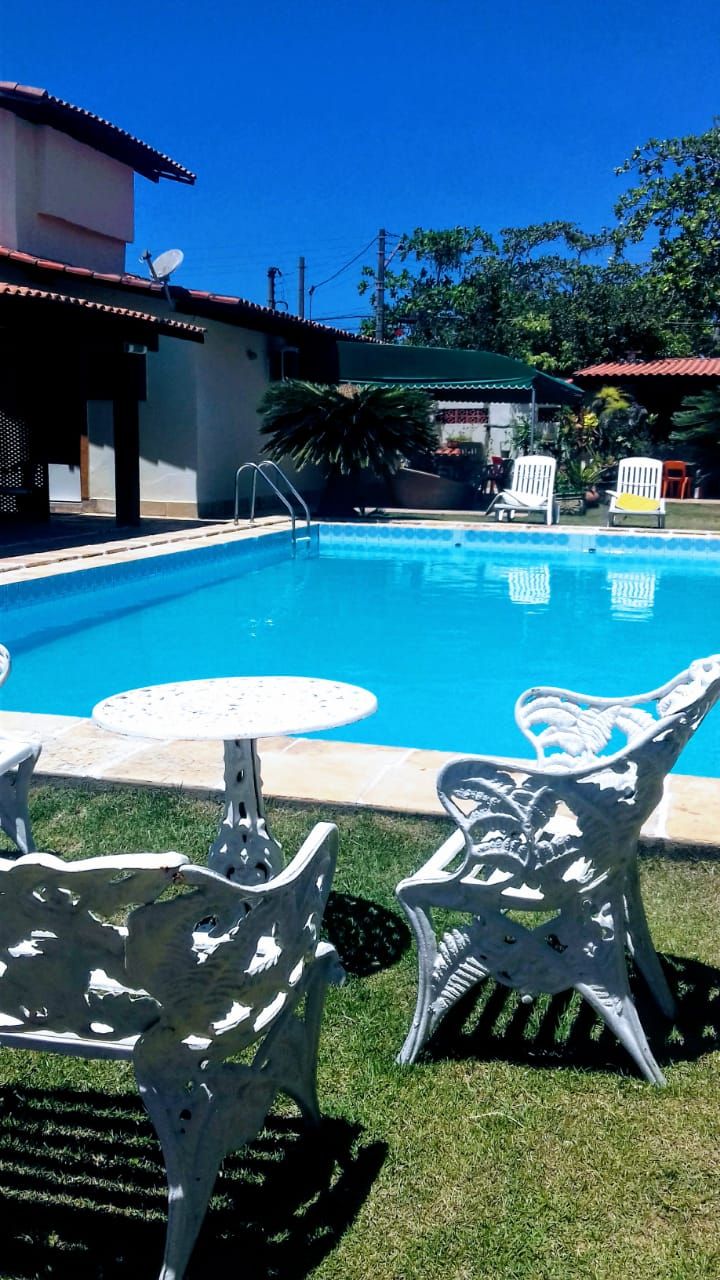 A swimming pool with a clear blue water surface, surrounded by white outdoor furniture and a building with a red roof.
