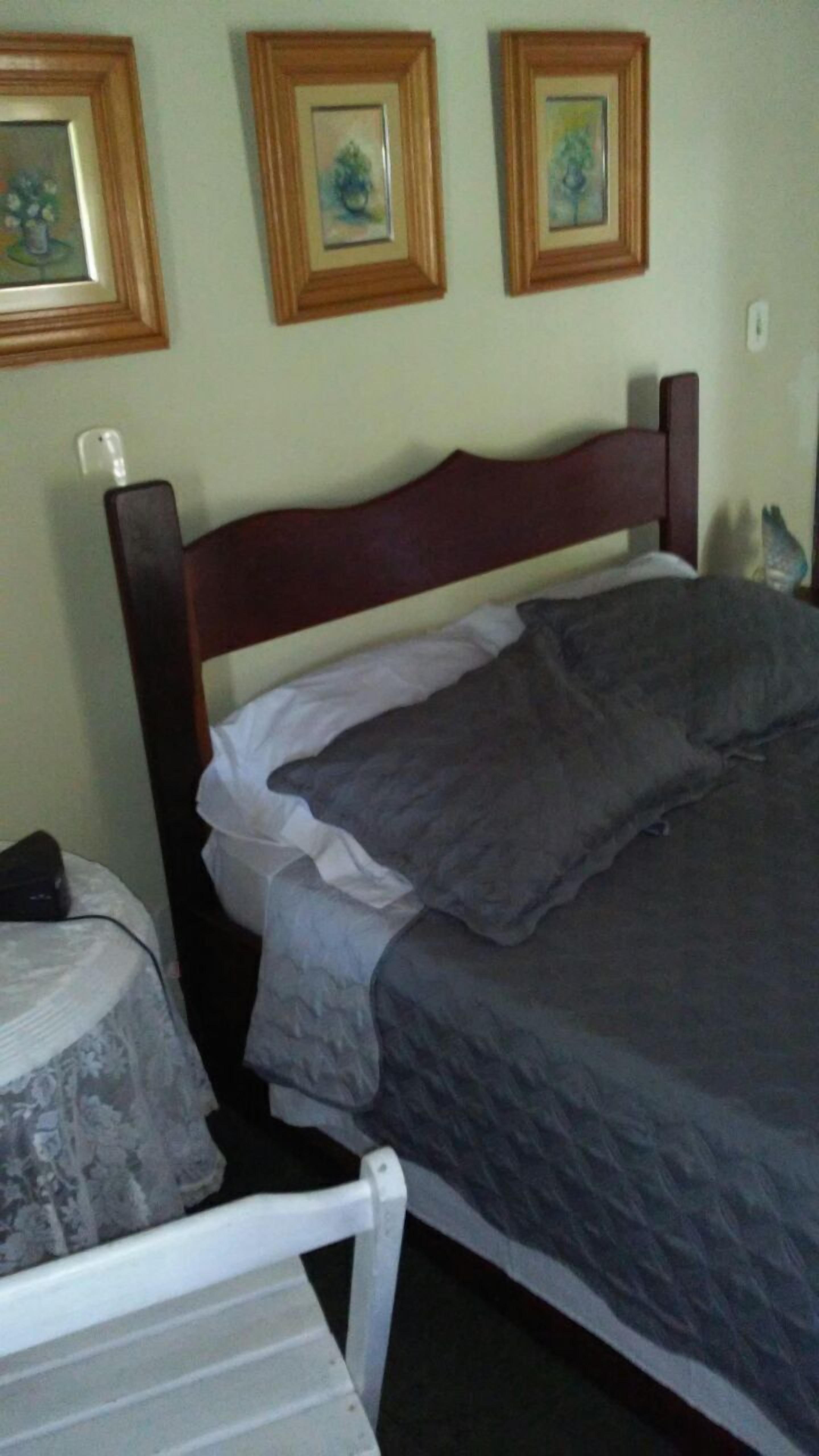 A bedroom with a wooden headboard, a bed with a gray blanket and pillows, a white chair, and two framed pictures on the wall.