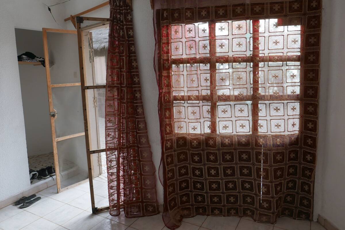 Una habitación con ventana cubierta por una cortina estampada, una escalera de madera y un par de zapatos en el suelo.