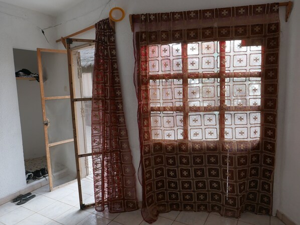 A room with a window covered by a patterned curtain, a wooden ladder, and a pair of shoes on the floor.