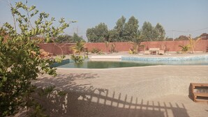 Una piscina con bordo piastrellato, circondata da un solarium in cemento, palme e un muro rosso.