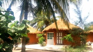 Un bungalow con tetto di paglia e un piccolo portico, circondato da palme e altra vegetazione tropicale.