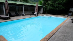 Une piscine dotée de chaises longues et de parasols, entourée d’une zone abritée surmontée d’un toit végétalisé.
