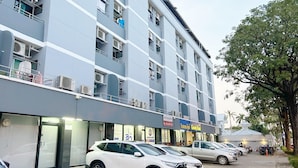 A multi-story hotel with several floors, air conditioning units on the balconies, and a row of parked cars in front. - Goody Hotel (Bangkok)