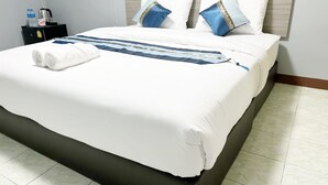 A neatly made bed with white bedding, two pillows with blue and gold accents, and a blue and gold decorative pillow on the headboard. - Goody Hotel (Bangkok)