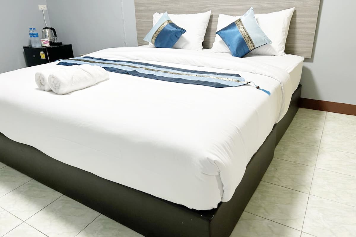 Un lit bien fait, avec une literie blanche, deux oreillers aux motifs bleus et dorés, et un coussin décoratif bleu et doré posé sur la tête de lit.