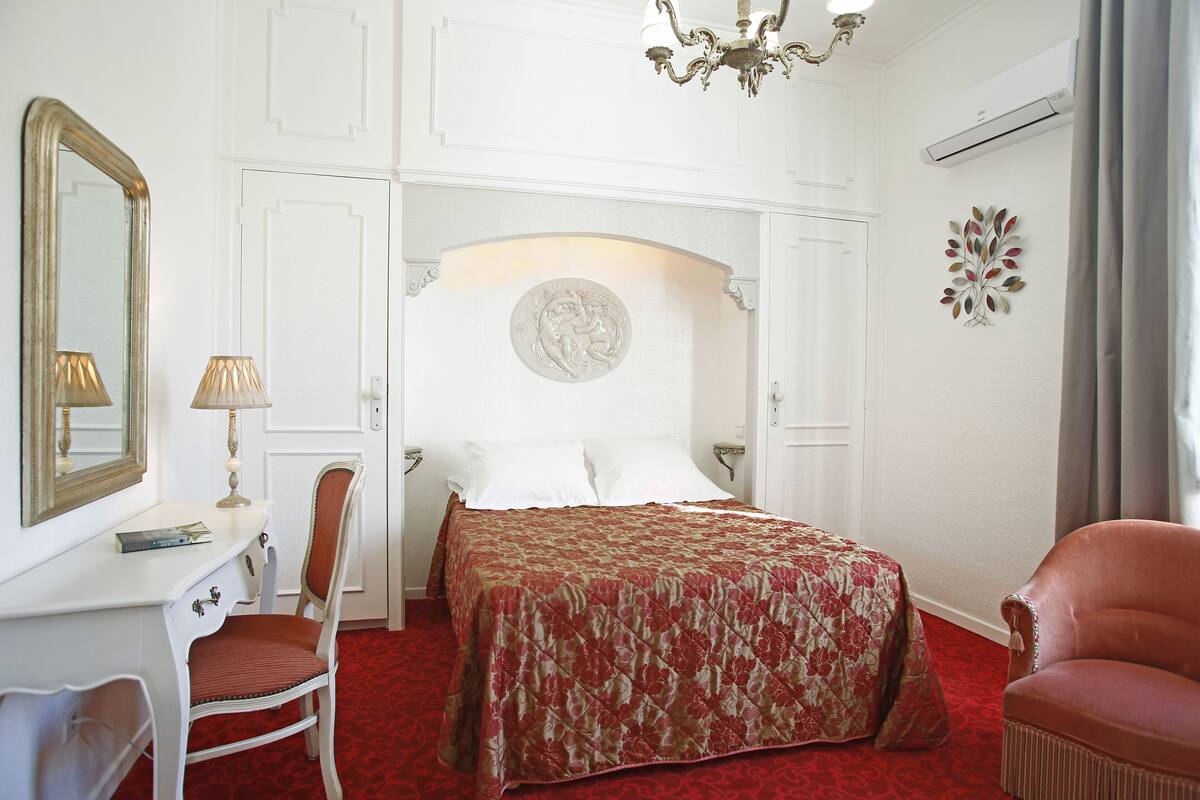 Een hotelkamer met een bed, een bureau, een stoel, een spiegel en een kroonluchter.