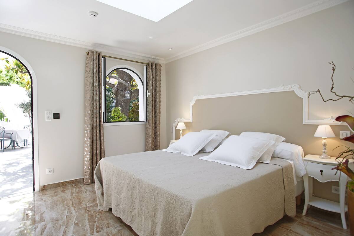 Een slaapkamer met een groot bed, een nachtkastje, een lamp en een raam met gordijnen.