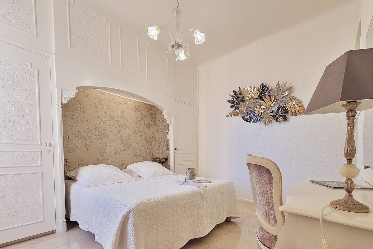 Een slaapkamer met een groot bed, een stoel, een bureau en een kroonluchter.