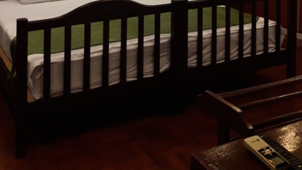 A bedroom with a wooden bed, white bedding, a brick-patterned wall, and a window with blinds. - Vanilla Hostel & Bar (Pattaya)