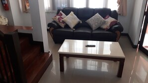 A living room with a black leather sofa, a white coffee table, and a remote control on it. - Vanilla Hostel & Bar (Pattaya)