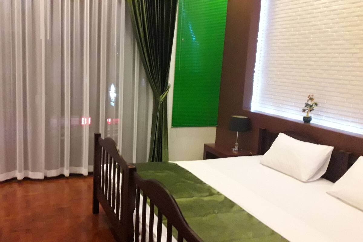 Quarto de hotel com cama, cadeira, mesa de cabeceira, abajur e janela com persianas.