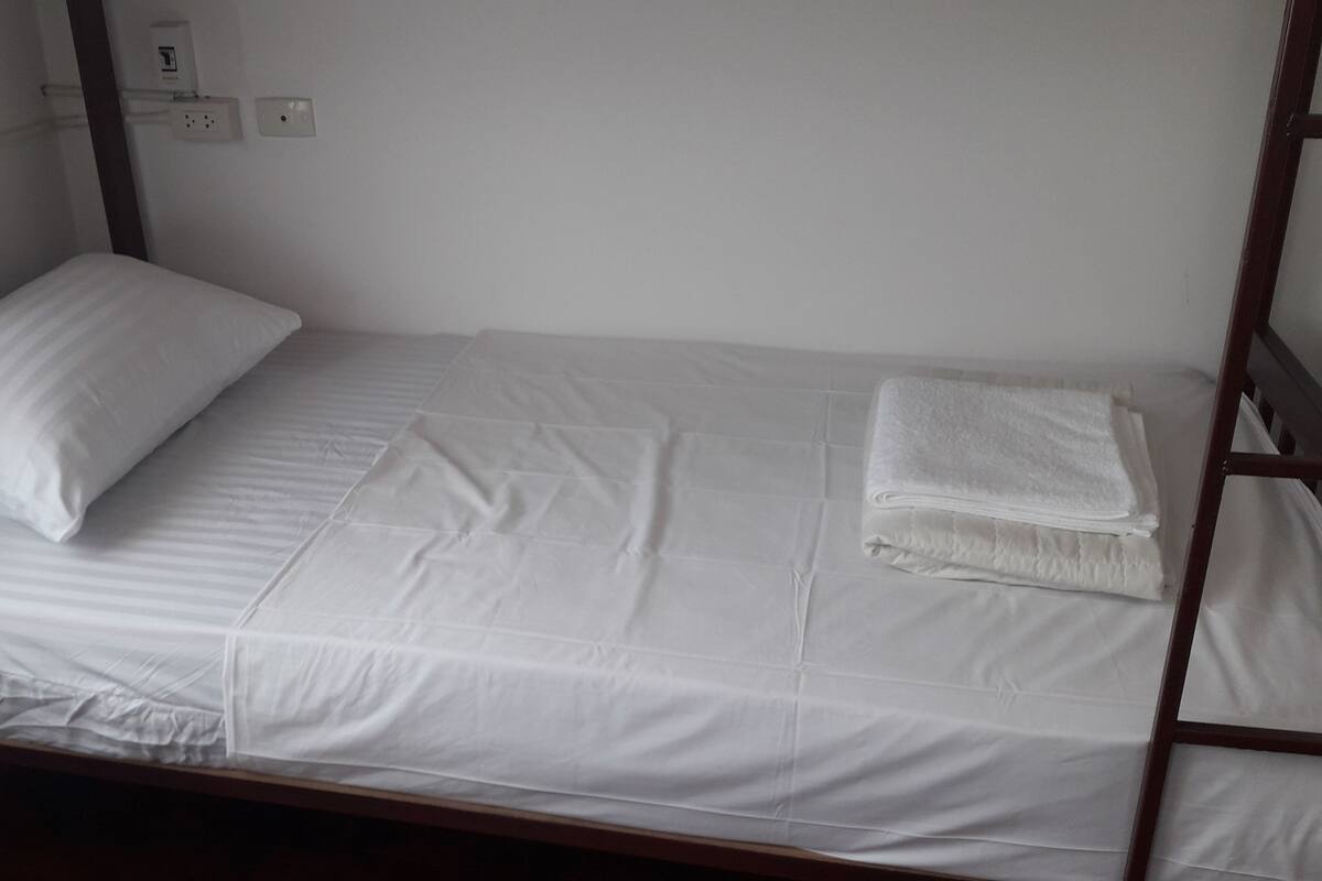 Uma cama de solteiro com roupa de cama branca, uma toalha dobrada e um travesseiro.