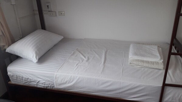 Una cama individual con sábanas blancas, una toalla doblada y un almohadón.
