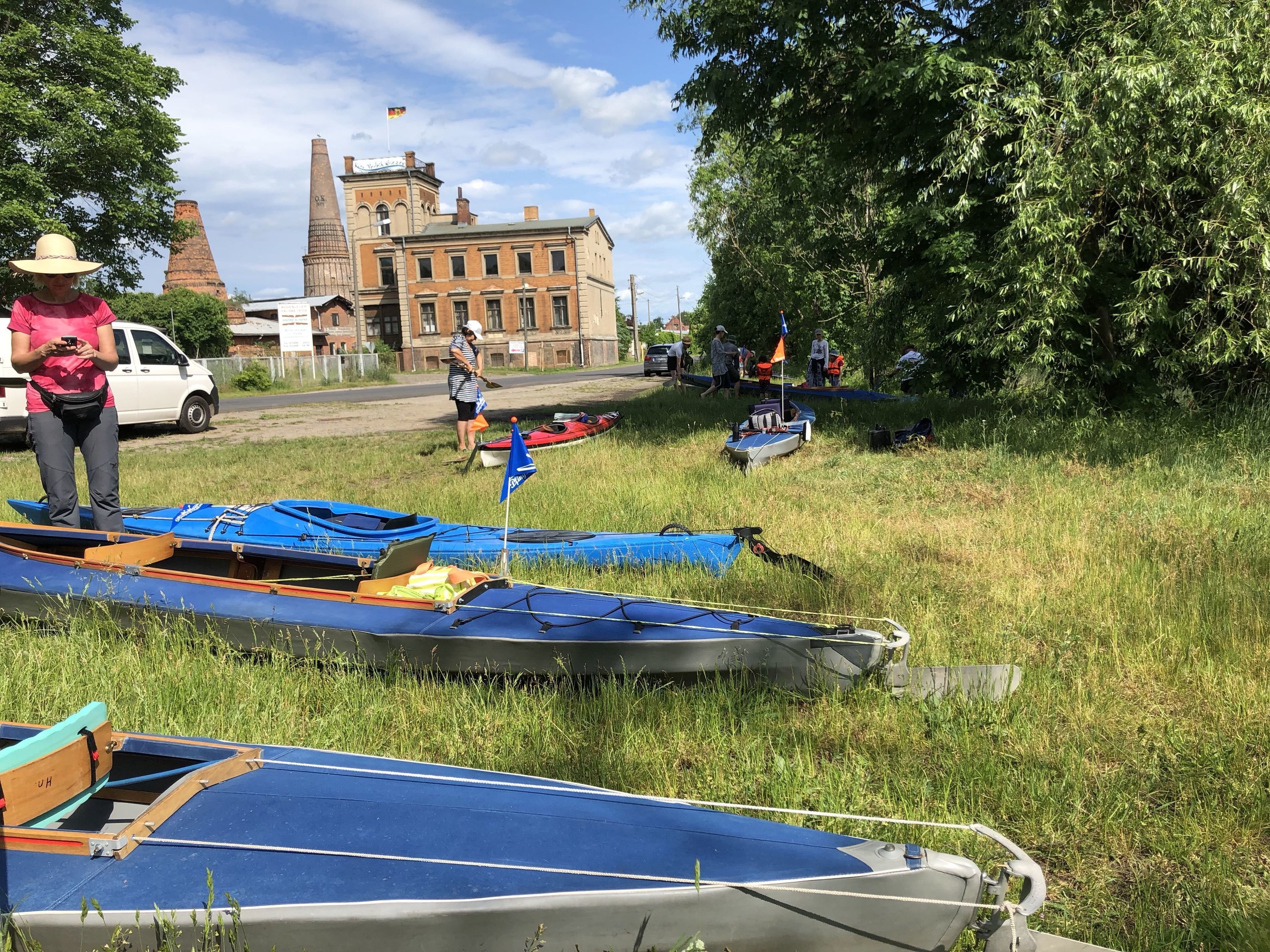 A grassy area with several boats, a white van, and a building with a flag in the background.