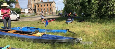 A grassy area with several boats, a white van, and a building with a flag in the background.