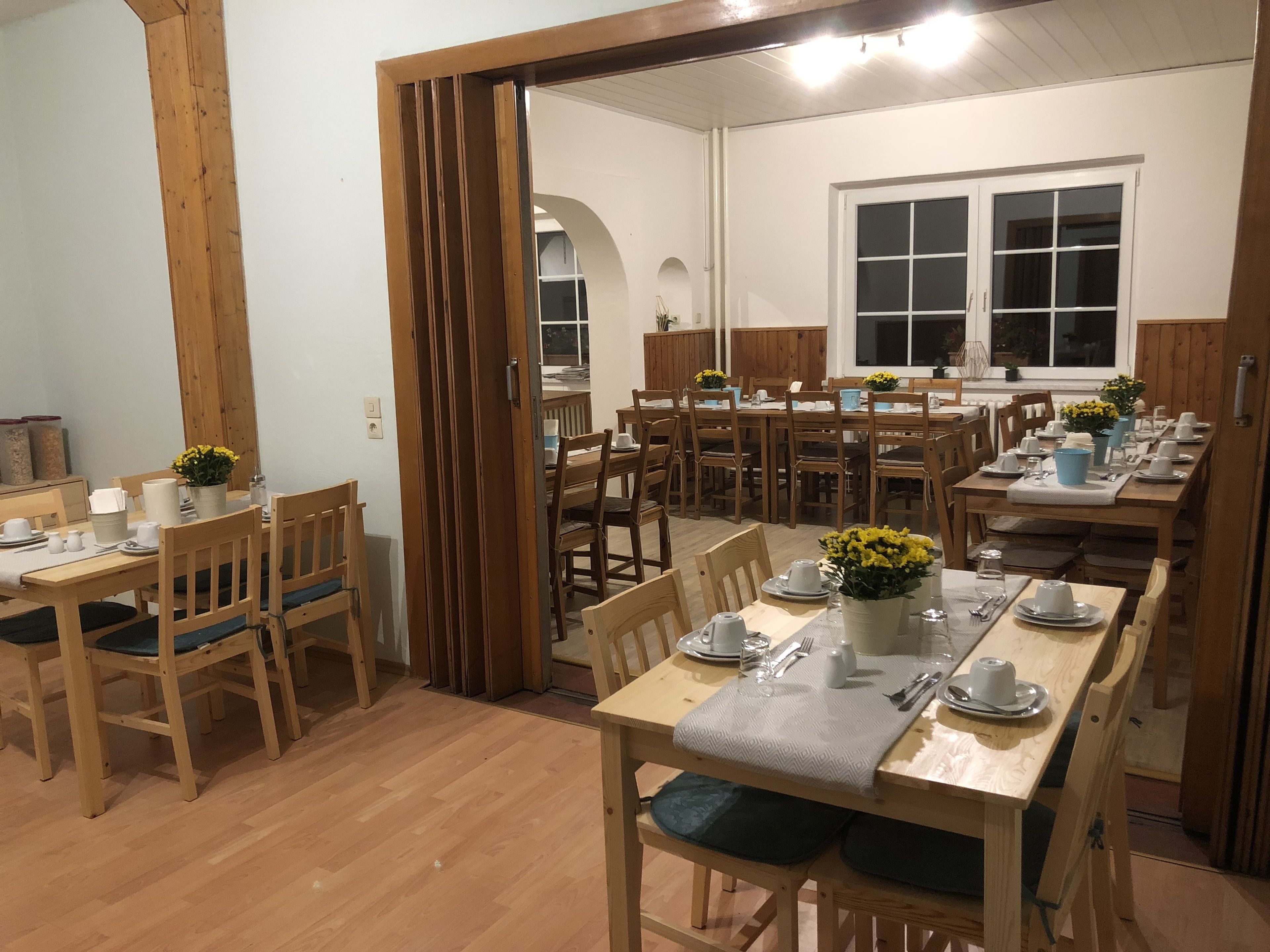 A dining area with wooden tables and chairs, a large window, and a view of the outside.