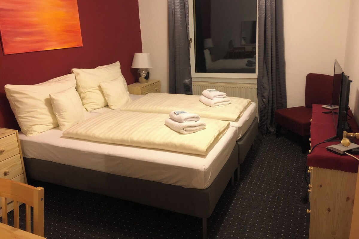 A hotel room with two beds, a desk, a chair, a TV, and a window with curtains.