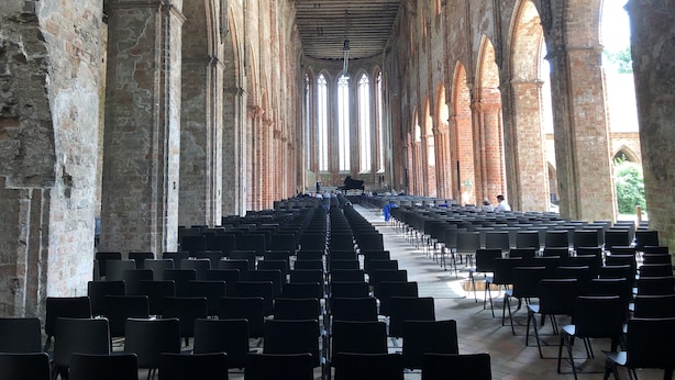 An interior with rows of black chairs, high arched brick walls, and large windows allowing natural light.