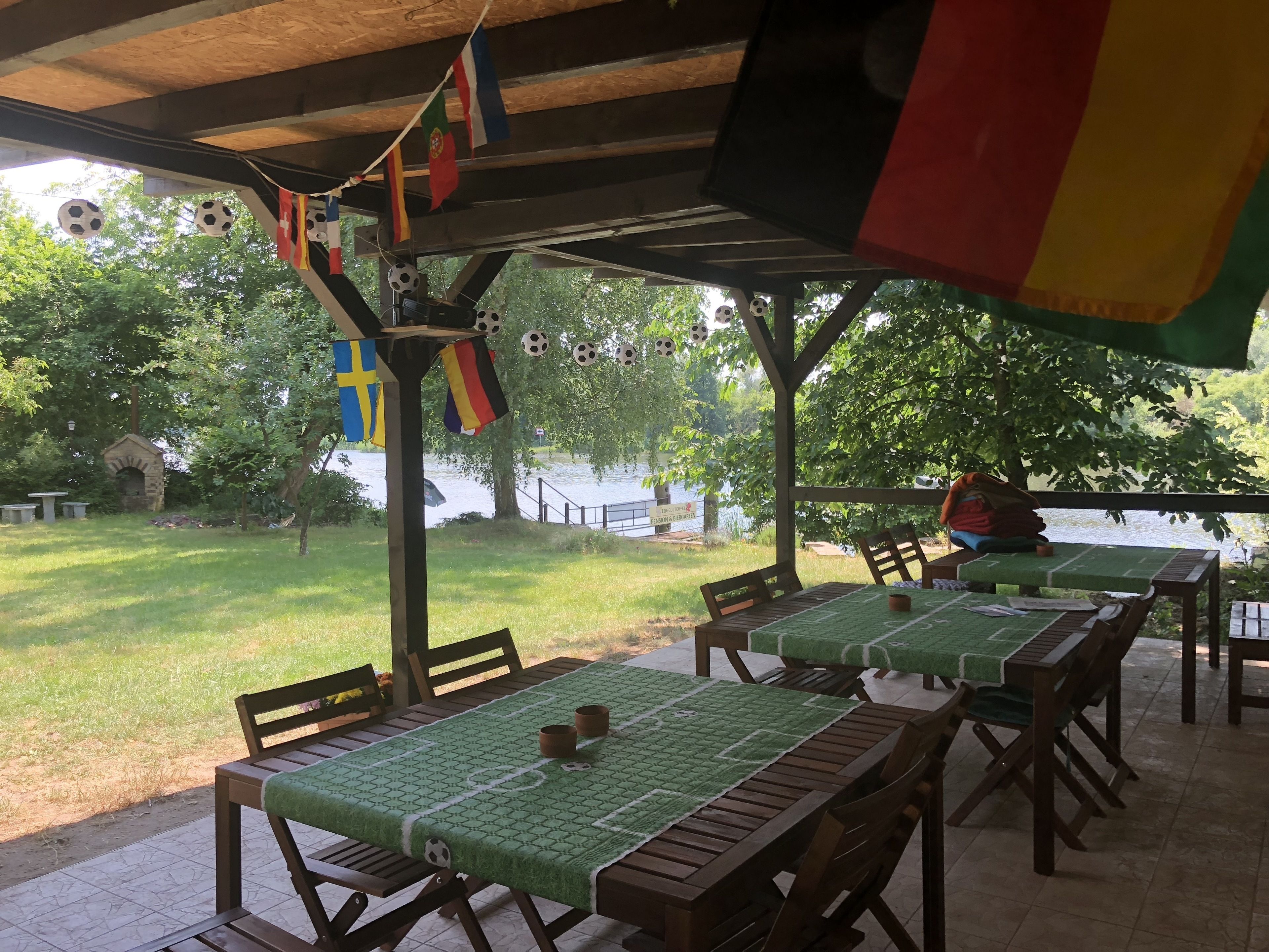 An outdoor patio area with tables and chairs, some covered with green tablecloths, and flags hanging from the ceiling.