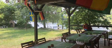 An outdoor patio area with tables and chairs, some covered with green tablecloths, and flags hanging from the ceiling.