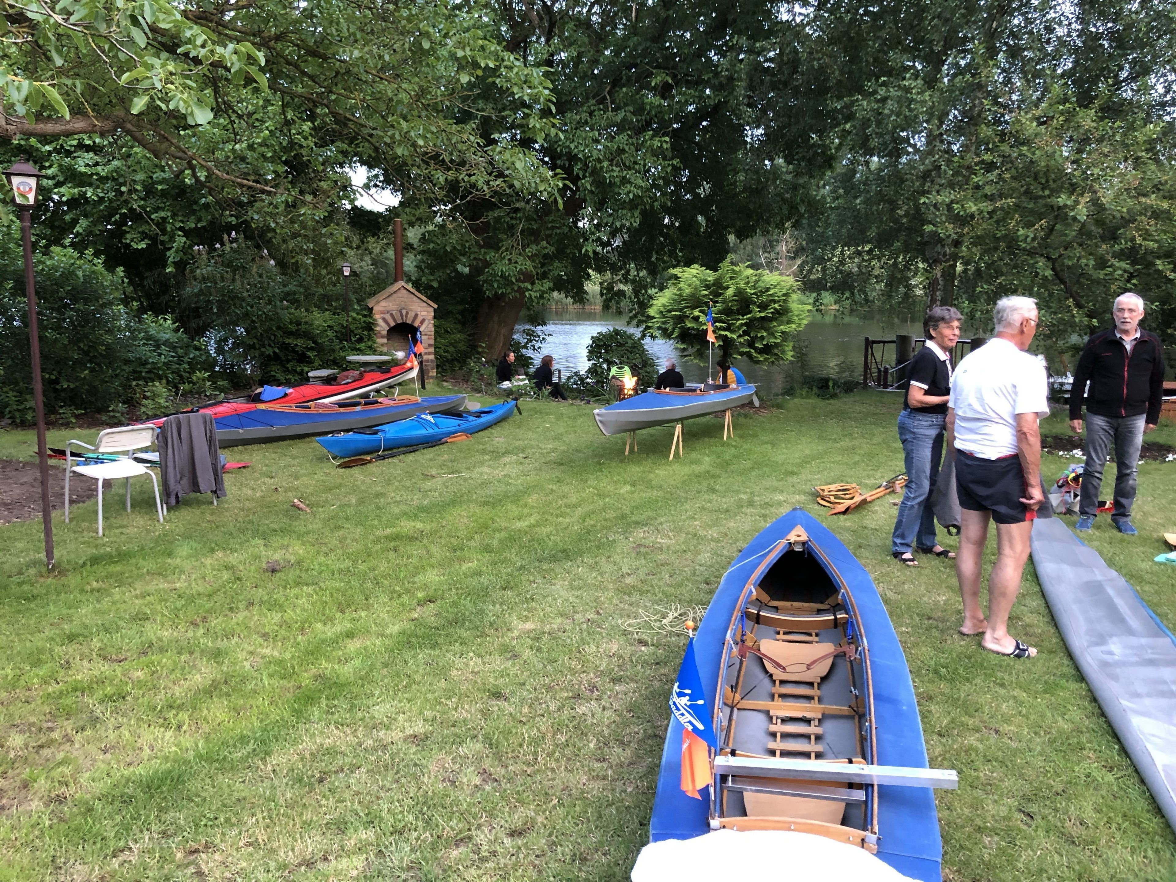 A grassy area with several canoes and kayaks, a brick structure, and a body of water in the background.