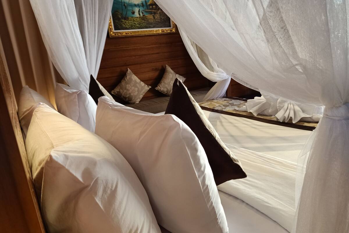 A bed with white linens and a canopy, a wooden headboard, and a painting on the wall.