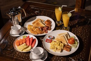 Une table de petit-déjeuner avec des assiettes remplies de nourriture, une cafetière et deux verres de jus d’orange.